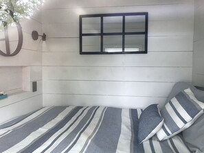 A bedroom with a bed, striped bedding, a window, and a wall-mounted light fixture. - Appalachian Container Cabin (Otto)