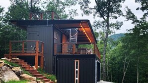 A modern cabin with a wooden deck, a spiral staircase, and a small enclosed porch. - Appalachian Container Cabin (Otto)