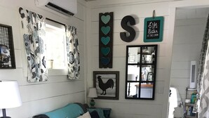 A cozy living room with a grey sofa, patterned curtains, a wooden floor, and a wall-mounted mirror. - Appalachian Container Cabin (Otto)