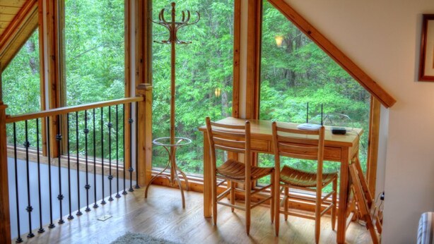 Ein Holzespeisesaal mit Stühlen in einem Zimmer mit großen Fenstern, die auf einen Wald blicken.