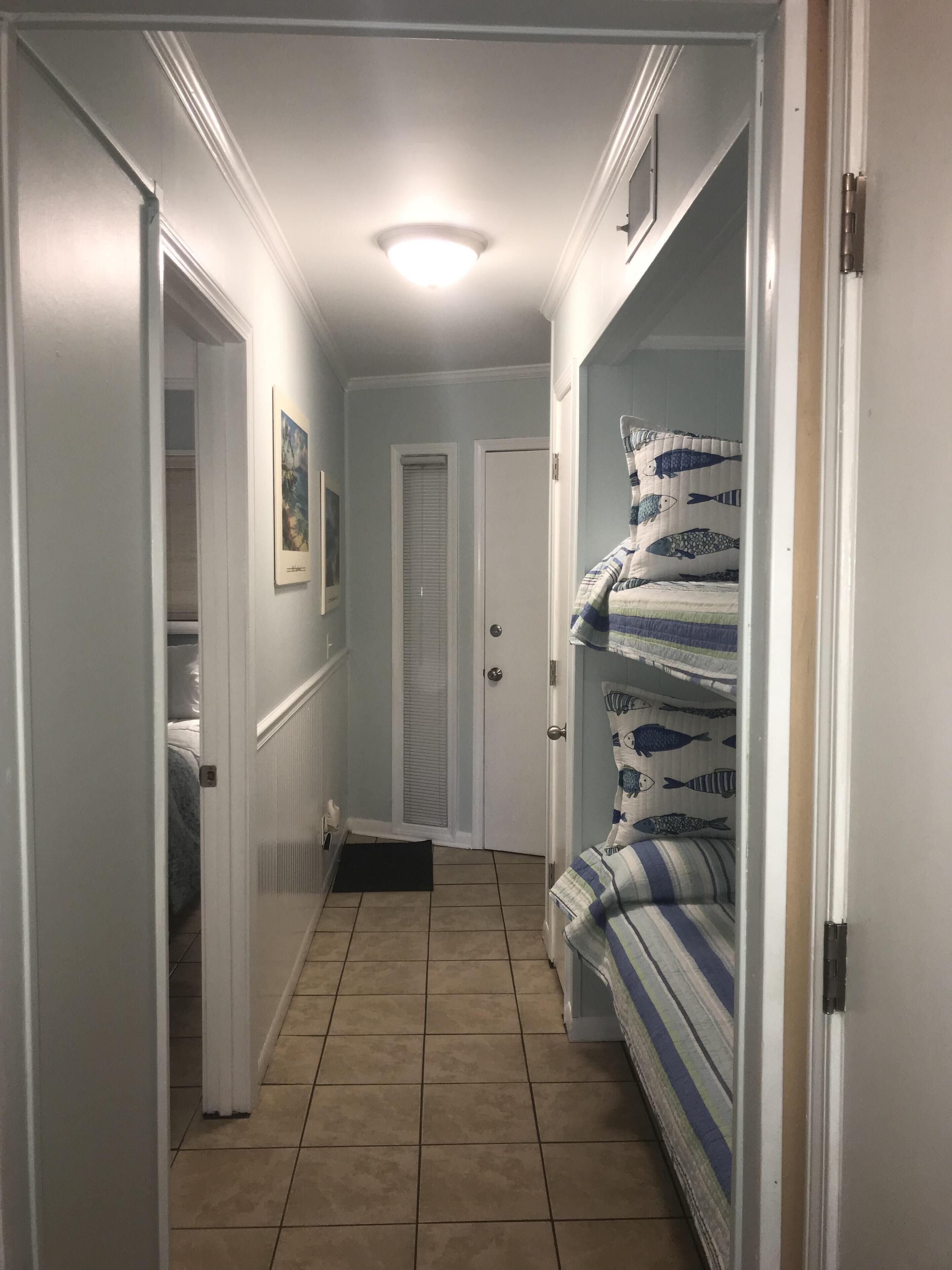 A narrow hallway with a tiled floor, a door at the end, and a bed with striped bedding on the right.
