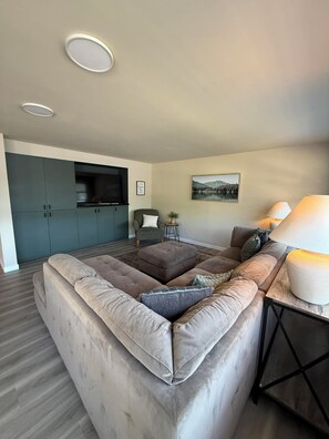 A modern living room with a sectional sofa, a television, a painting, and a lamp.