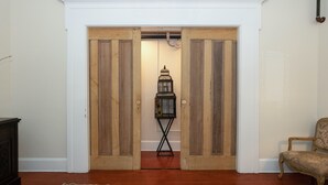 Ein Zimmer mit Holztür, Vogelkäfig auf Ständer, Stuhl und Teppich mit Muster.
