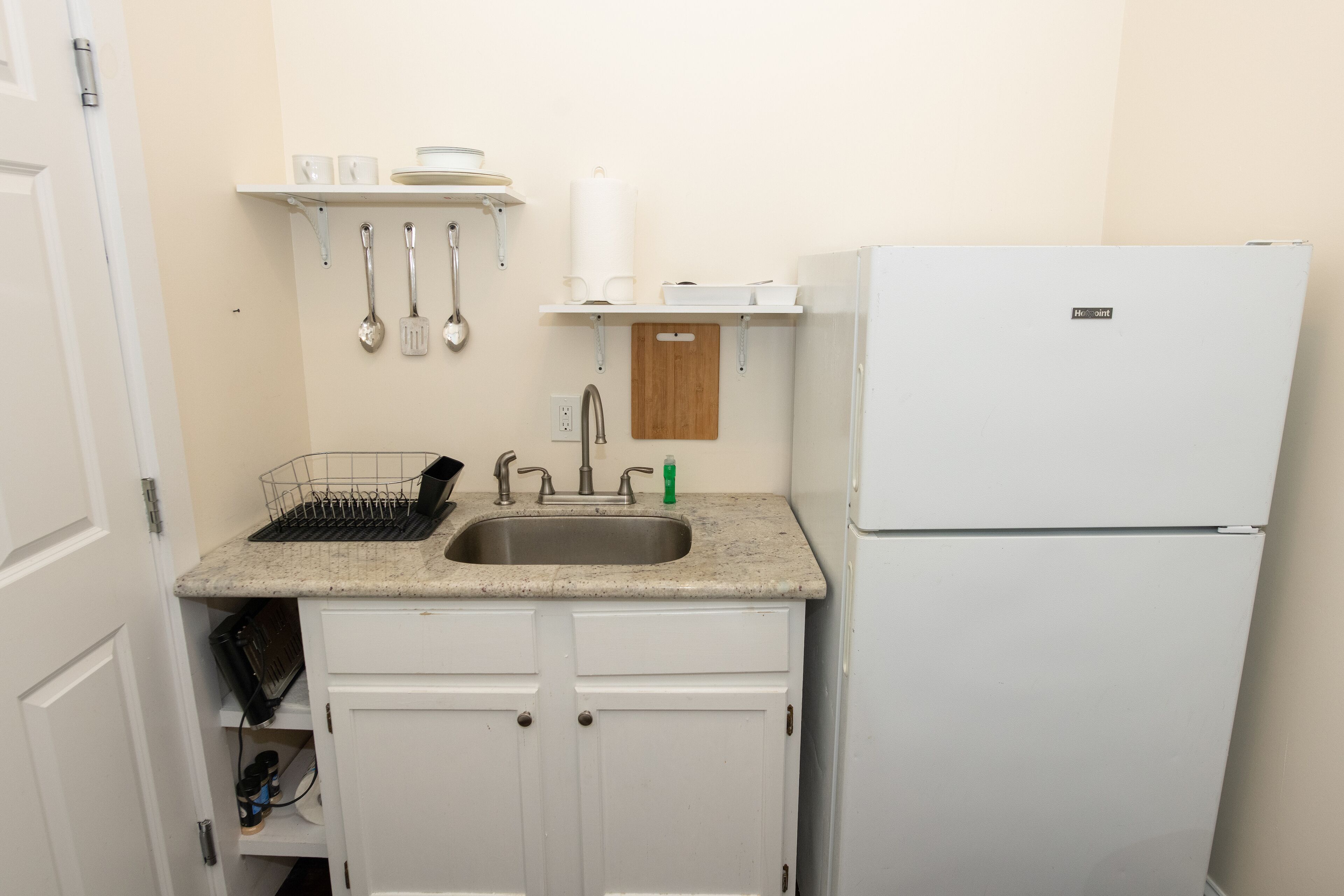 A compact kitchen with a sink, a white refrigerator, and a wooden cutting board on the countertop.