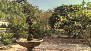 Ein Steinfountain in einem gärtnerisch angelegten Garten mit Backsteinpflaster, Bäumen und einem Zaun im Hintergrund.