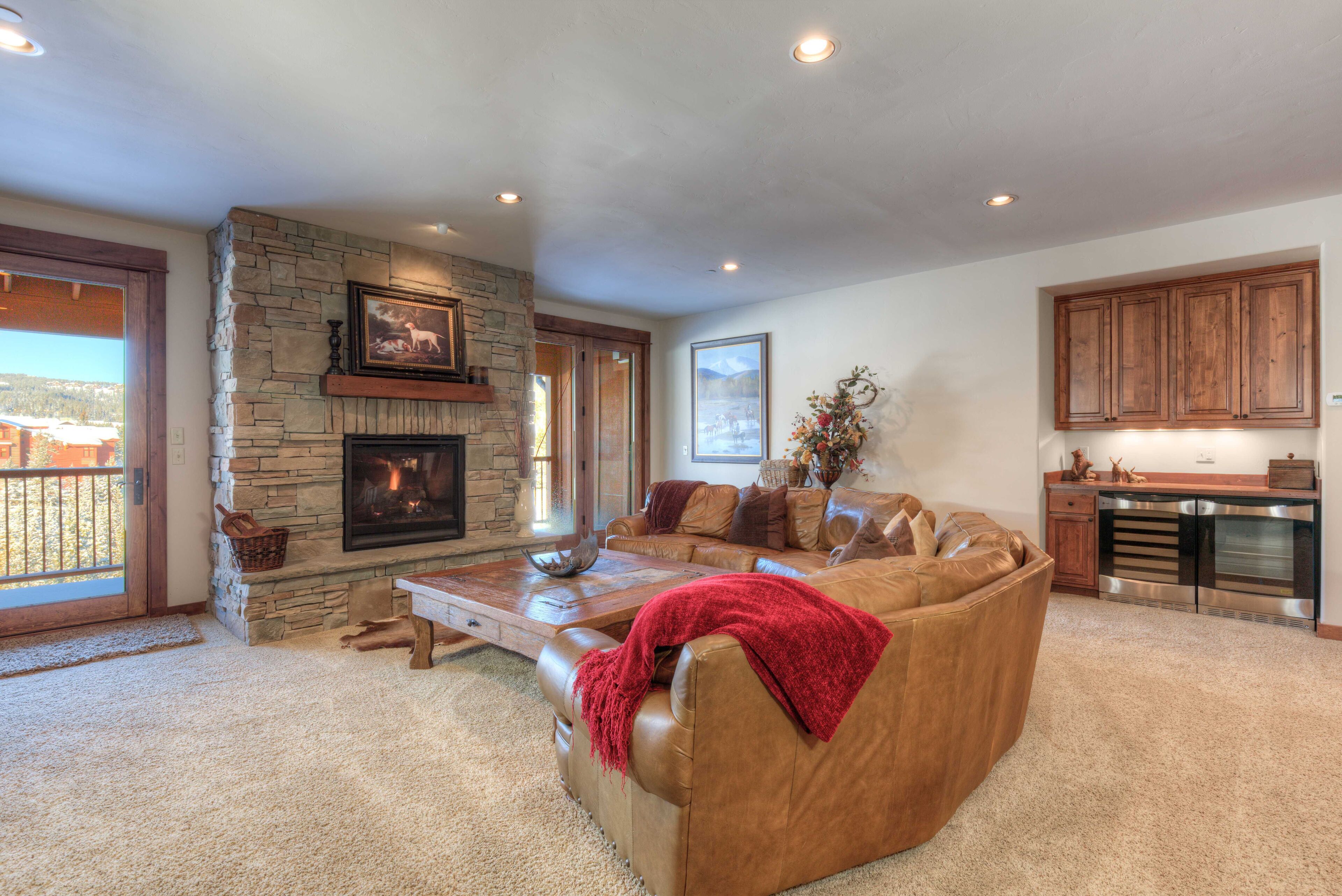 A spacious living room with a stone fireplace, leather sofa, and a view of the outdoors.