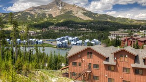 A lodge with multiple wooden cabins, a lake, and a mountain backdrop.