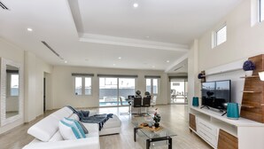 Un salon spacieux avec un canapé blanc, une table basse en verre et un téléviseur posé sur un meuble en bois.