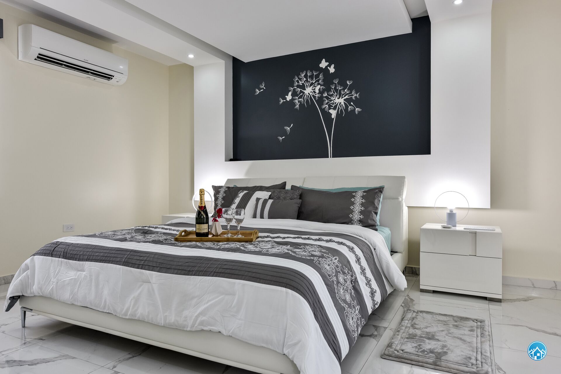 A modern bedroom with a bed, bedside tables, a nightstand, and a wall-mounted air conditioner.