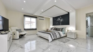 Une chambre moderne avec un grand lit, une télévision, un fauteuil massant et une grande fenêtre.