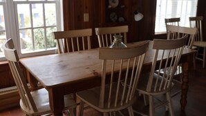 A dining area with a wooden table and chairs, a window with blinds, and a shelf with decorative plates. - Oceanfront 4BR 2 Story Duplex with Private Beach Access (Carolina Beach)