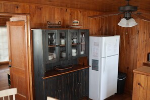 Uma cozinha com paredes de madeira, geladeira, armário com portas de vidro e ventilador de teto.