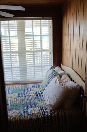 Quarto com cama, janela com persianas e paredes de madeira.