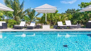 A swimming pool with lounge chairs and umbrellas, surrounded by tropical vegetation. - Sea La Vie - Beachside 1 Bedroom Unit #6 (Providenciales)