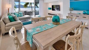 A modern hotel room with a dining area, a sofa set, a TV, and a view of the ocean. - Frangipani Lodge 106, Beachfront Apartment on Hamilton Island (Hamilton Island)
