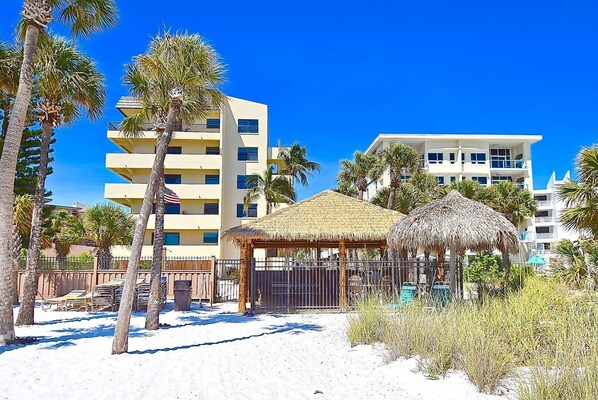 A beachside hotel with multiple-story buildings, a thatched-roof structure, and palm trees.