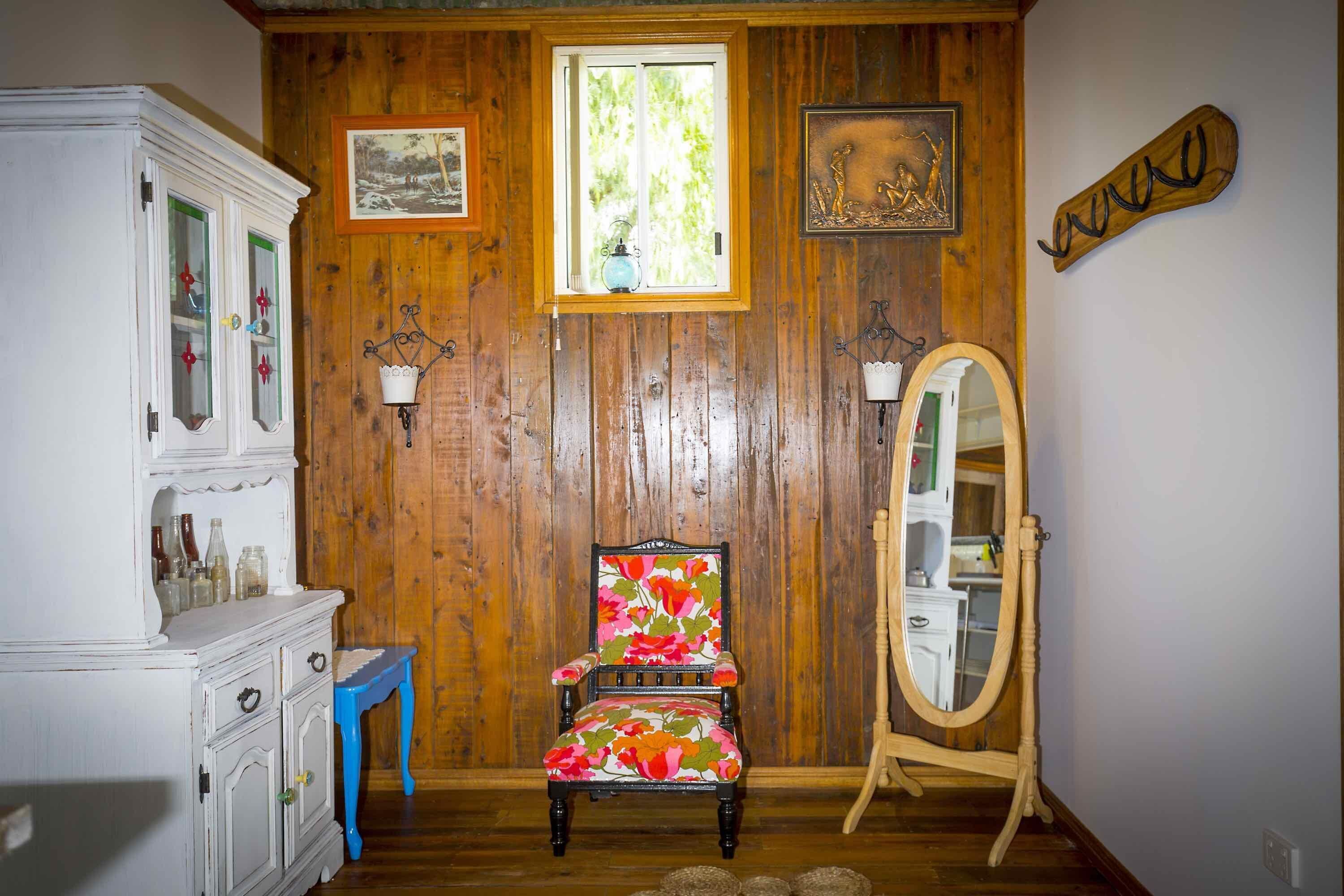 A room with wooden paneling, a floral chair, a white cabinet, a mirror, and a window with a view of greenery.