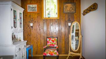 A room with wooden paneling, a floral chair, a white cabinet, a mirror, and a window with a view of greenery.