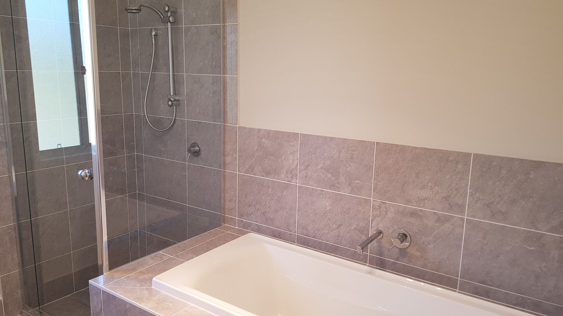 Une salle de bain avec une douche à parois de verre, une baignoire et des murs carrelés.