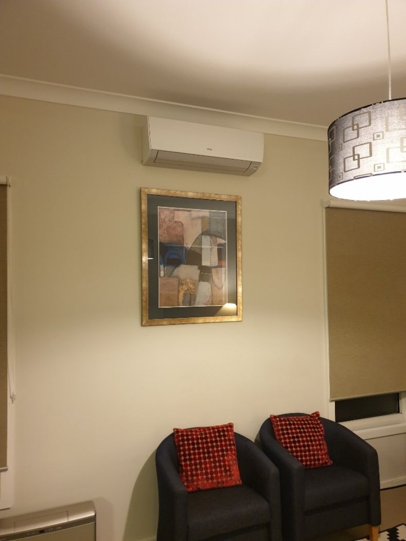Una habitación con dos sillones negros, un cuadro abstracto enmarco y una lámpara colgante moderna.
