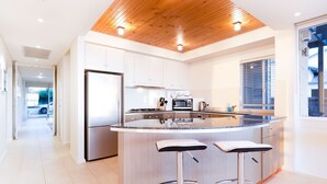 Een moderne keuken met een centraal eiland, roestvrijstalen apparatuur en een houten plafond.