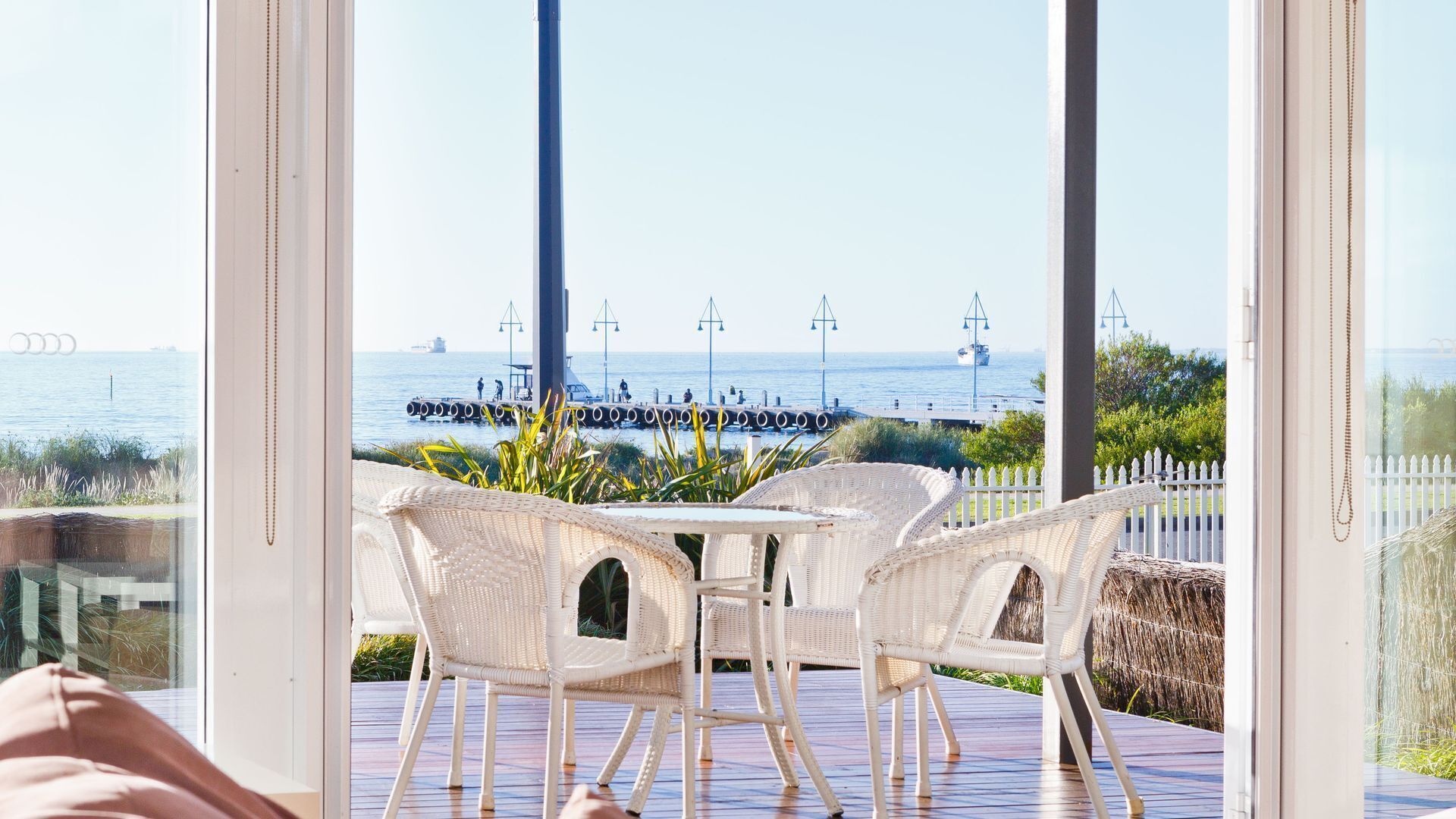 A view from a room with a large window overlooking a dock and the sea.