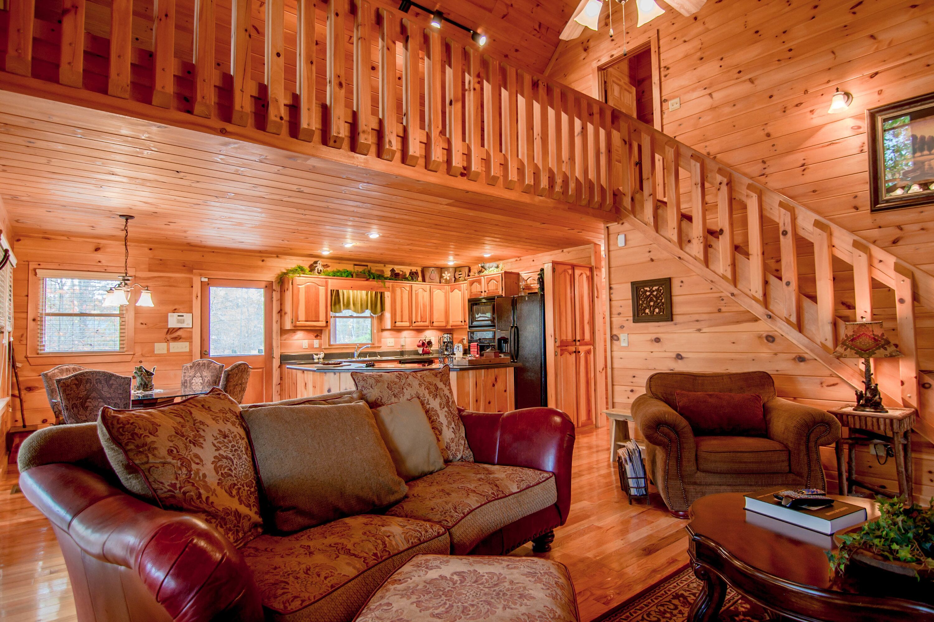 A wooden cabin interior with a living room, kitchen, and staircase.