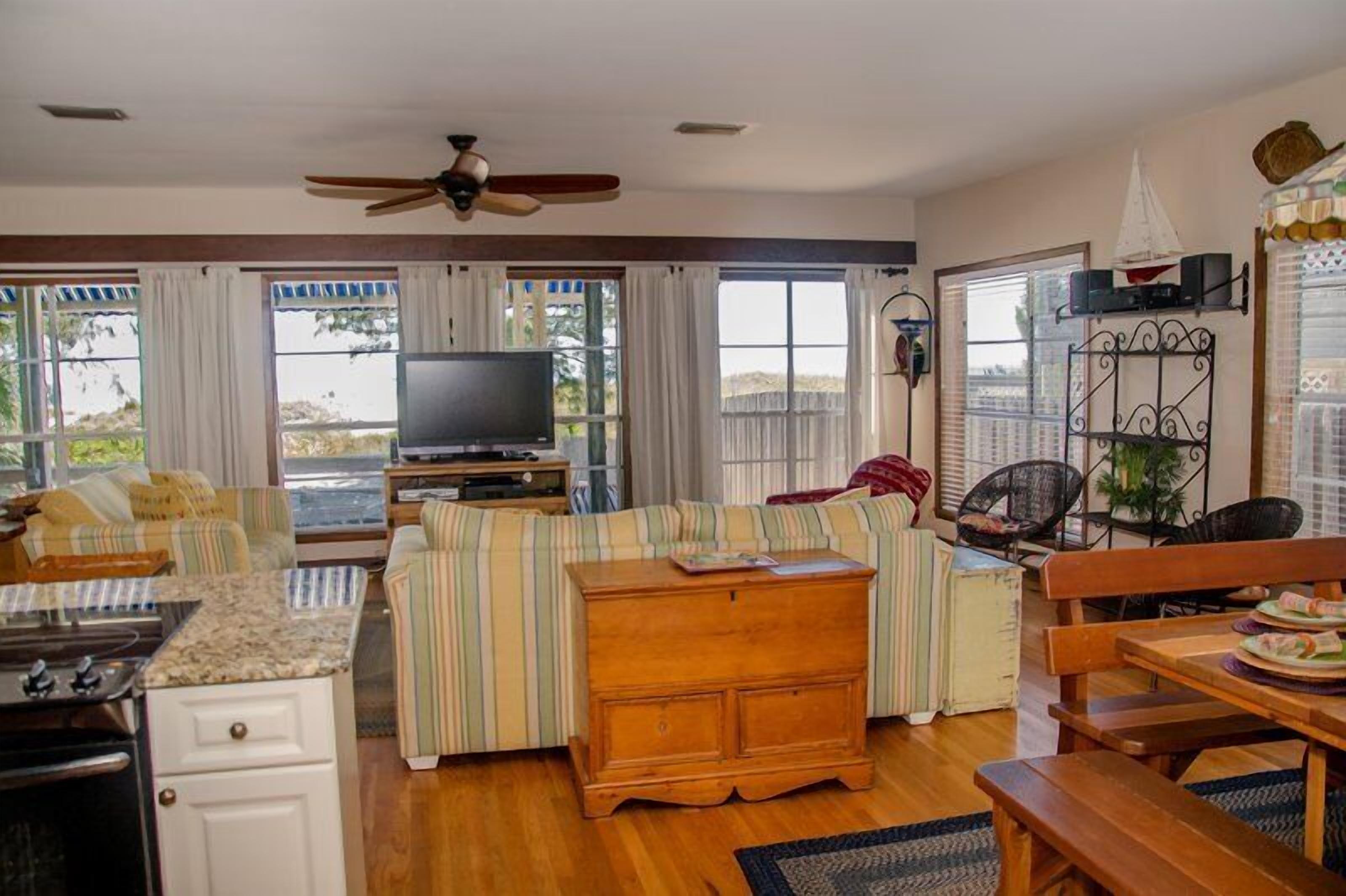 Una sala de estar acogedora con televisor, sofá a rayas, mueble de madera y un comedor con mesa y bancos.
