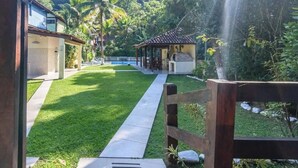 A pathway leading to a building with a covered outdoor area, surrounded by lush greenery and a small waterfall.