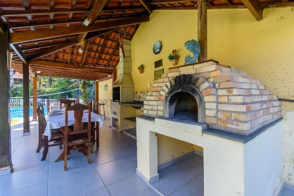An outdoor patio with a brick oven, wooden chairs, and a table set for dining.