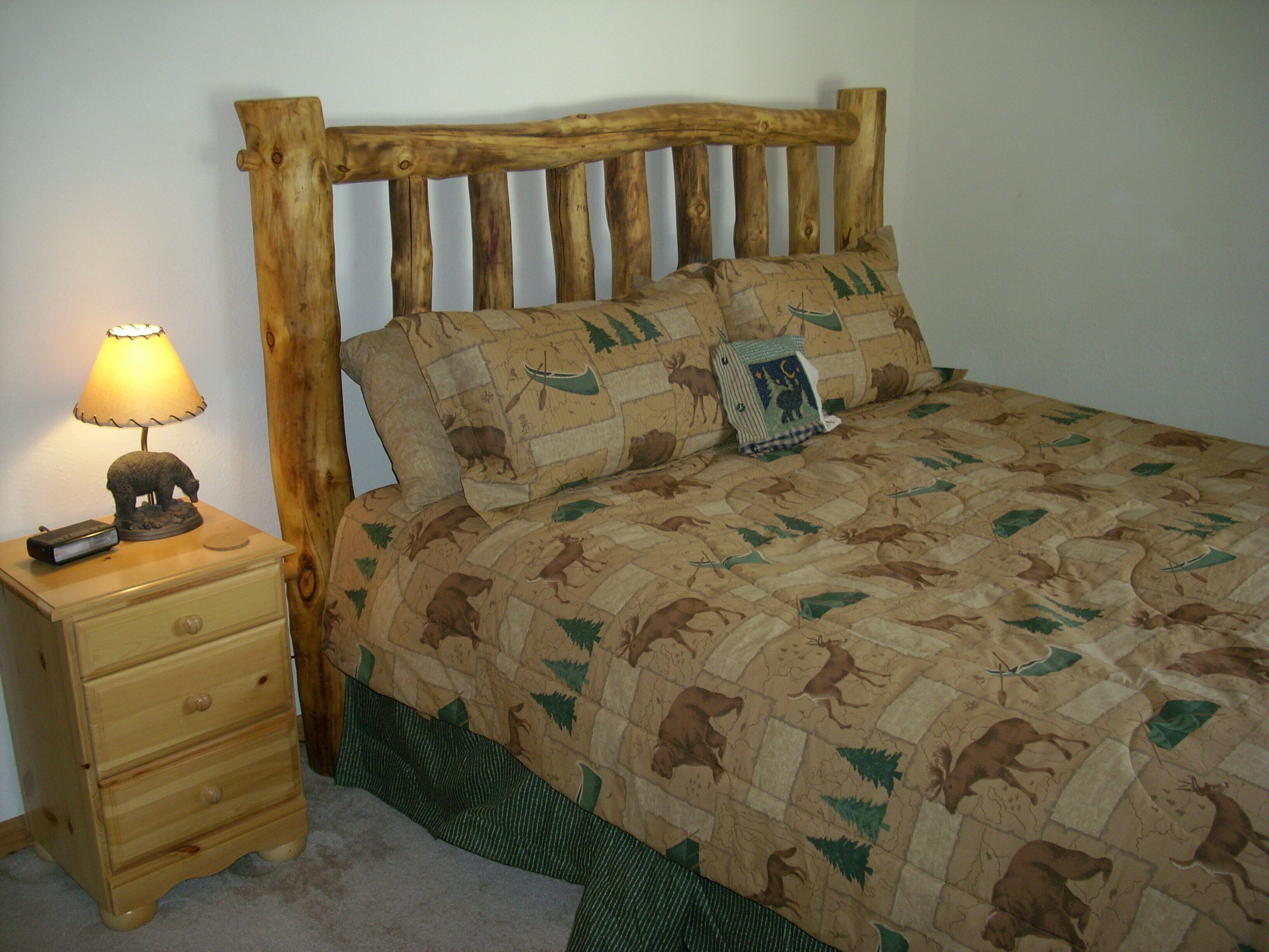 Uma cama com cabeceira acolchoada, uma mesa de cabeceira com abajur e uma gaveta.