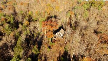 An aerial view of a house surrounded by dense forest with autumn foliage.