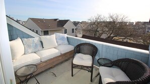 Ein Balkon mit einer weißen Couch, Korbstühlen und einem kleinen Tisch.