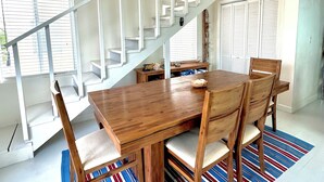 Een eetgedeelte met een houten tafel en stoelen, een gestreept vloerkleed, een trap met witte leuningen en een decoratief wandobject.