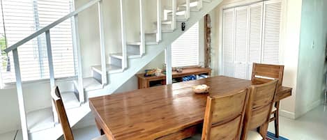 Un coin repas avec une table et des chaises en bois, un tapis à rayures, un escalier avec des rampes blanches et un élément décoratif mural.