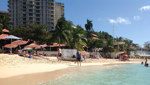 A beach with people sunbathing, umbrellas, and a lifeguard tower.