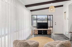 A modern living room with a flat-screen TV, wooden entertainment unit, and plush poufs. - The Place - Pool, Lake, Kayaks & much more! (Gwandalan)