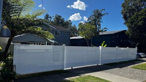 Un quartier résidentiel avec une clôture blanche, une maison dotée d’un garage et un ciel d’un bleu limpide.