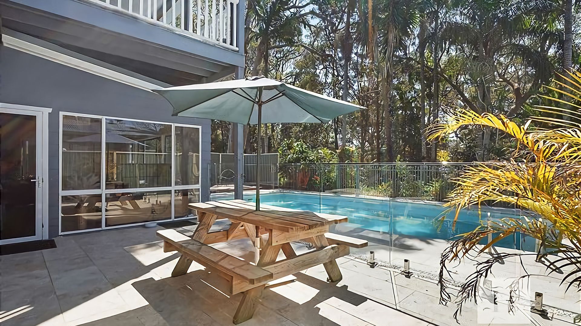 Una casa moderna con puerta de cristal, mesa y banco de madera, y una piscina.