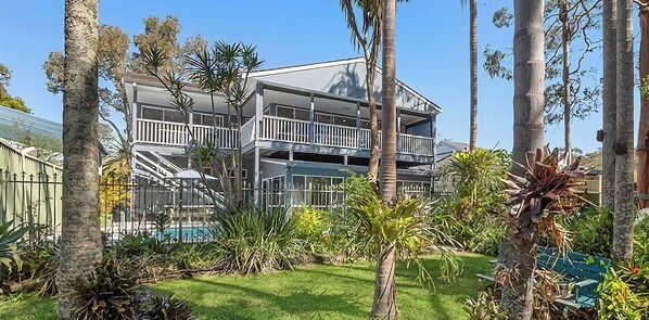 Un bâtiment à deux étages doté de balcons, entouré de palmiers et agrémenté d’une piscine.