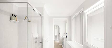 Un baño moderno con cabina de ducha de vidrio, pared con azulejos blancos y estante empotrado con artículos de aseo.