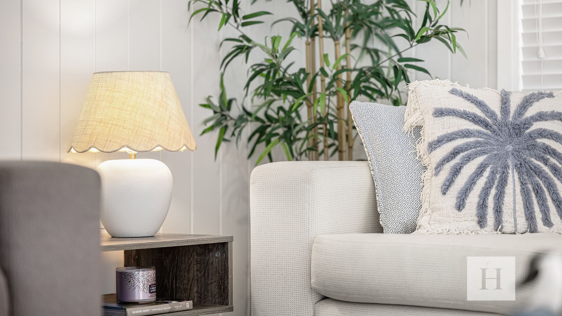 A modern living room with a white sofa, a lamp, and a plant.