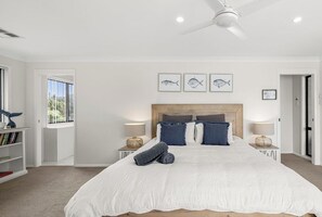 Une chambre à coucher avec un grand lit, deux tables de chevet, un ventilateur de plafond et des œuvres d’art encadrées accrochées au mur.