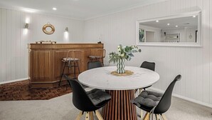 Un coin repas avec une table ronde, des chaises noires, un bar en bois et un miroir au mur.