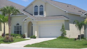 A two-story house with a garage, a covered driveway, and a well-maintained lawn.
