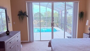 A bedroom with a bed, a dresser, a ceiling fan, and a sliding glass door leading to a pool area.