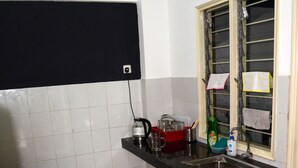A compact kitchen with a black countertop, a window with a towel hanging, and a yellow tablecloth on a chair.