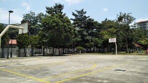 An outdoor basketball court with a fence, trees, and a building in the background.