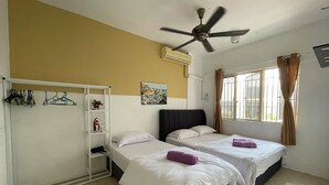 A hotel room with two beds, a ceiling fan, an air conditioning unit, a window with curtains, and a wall-mounted shelf with clothes and a small plant.