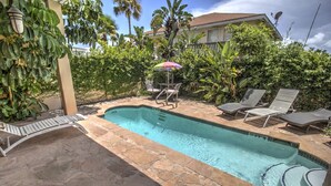 A swimming pool with stone tiles, surrounded by lush greenery and a few lounge chairs.